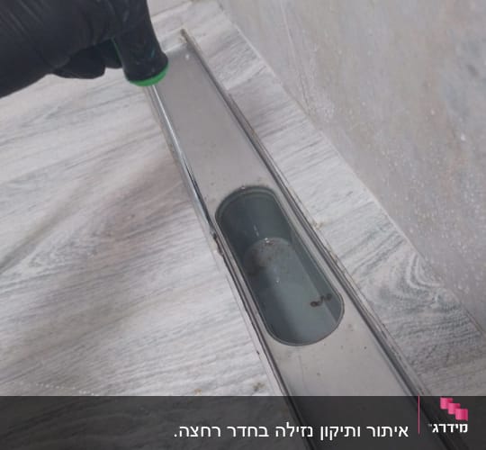 יד עם כפפה מחזיקה כלי ליד תעלת ניקוז